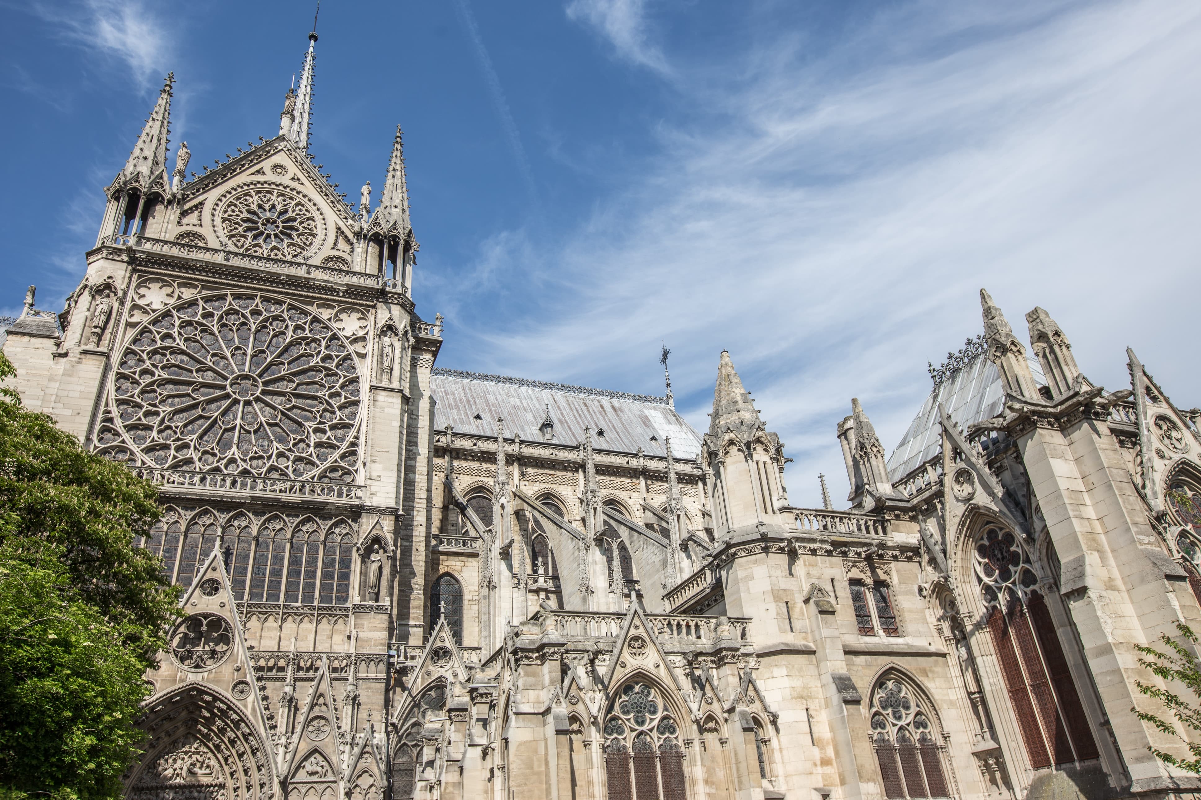 View of the side of Notre Dame cathedral on a sunny day.  Notre Dame looks large and imposing, filling the whole image.